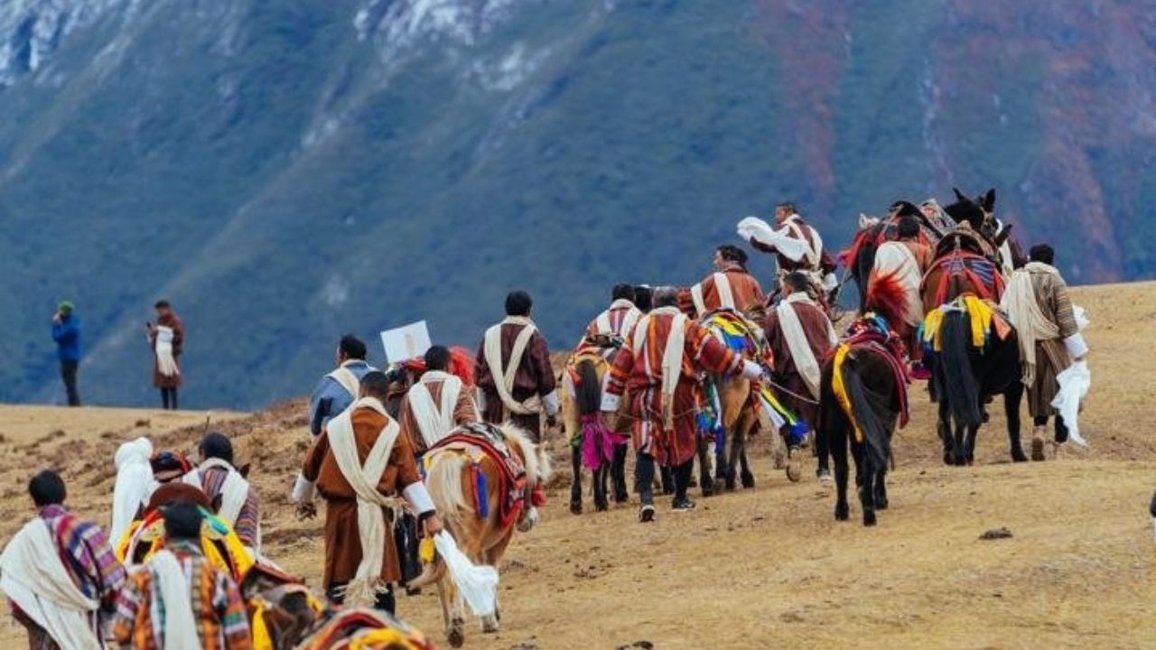 People in traditional dress walking with horses along a mountain trail.