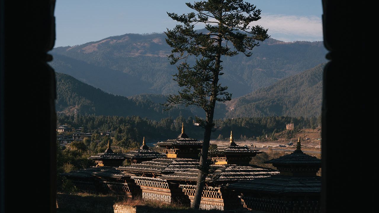 Ancient Bhutanese temple complex framed by an arched window, with mountains in the background.
