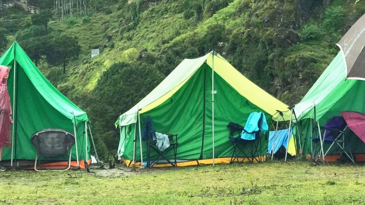 Green camping tents below a cliffside monastery in Bhutan.