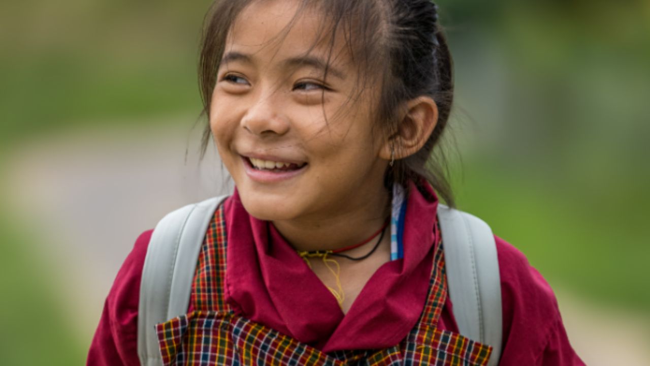 Smiling Bhutanese child wearing traditional dress on a village path.