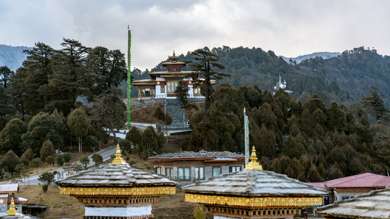 Hilltop Buddhist temple surrounded by forested mountains and prayer structures.