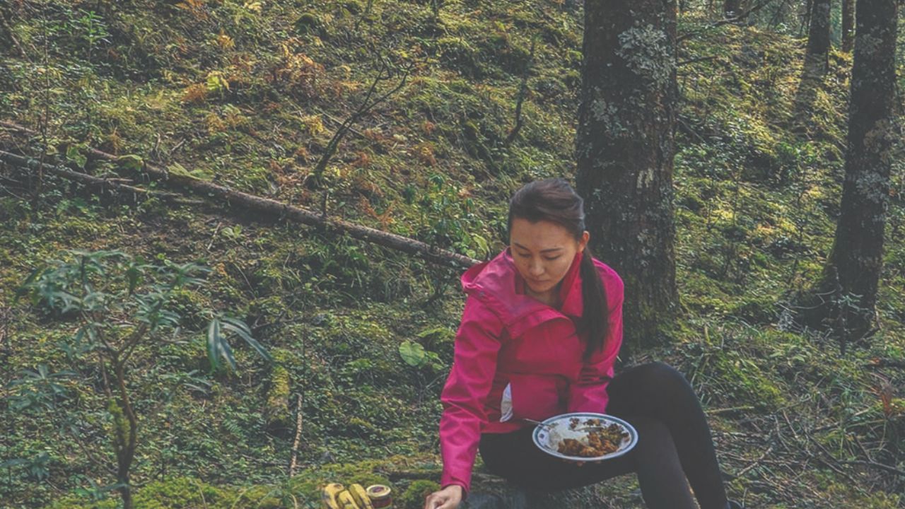 Woman enjoying nature on the Druk Path trekking trail in Bhutan while taking a break to prepare a meal outdoors.