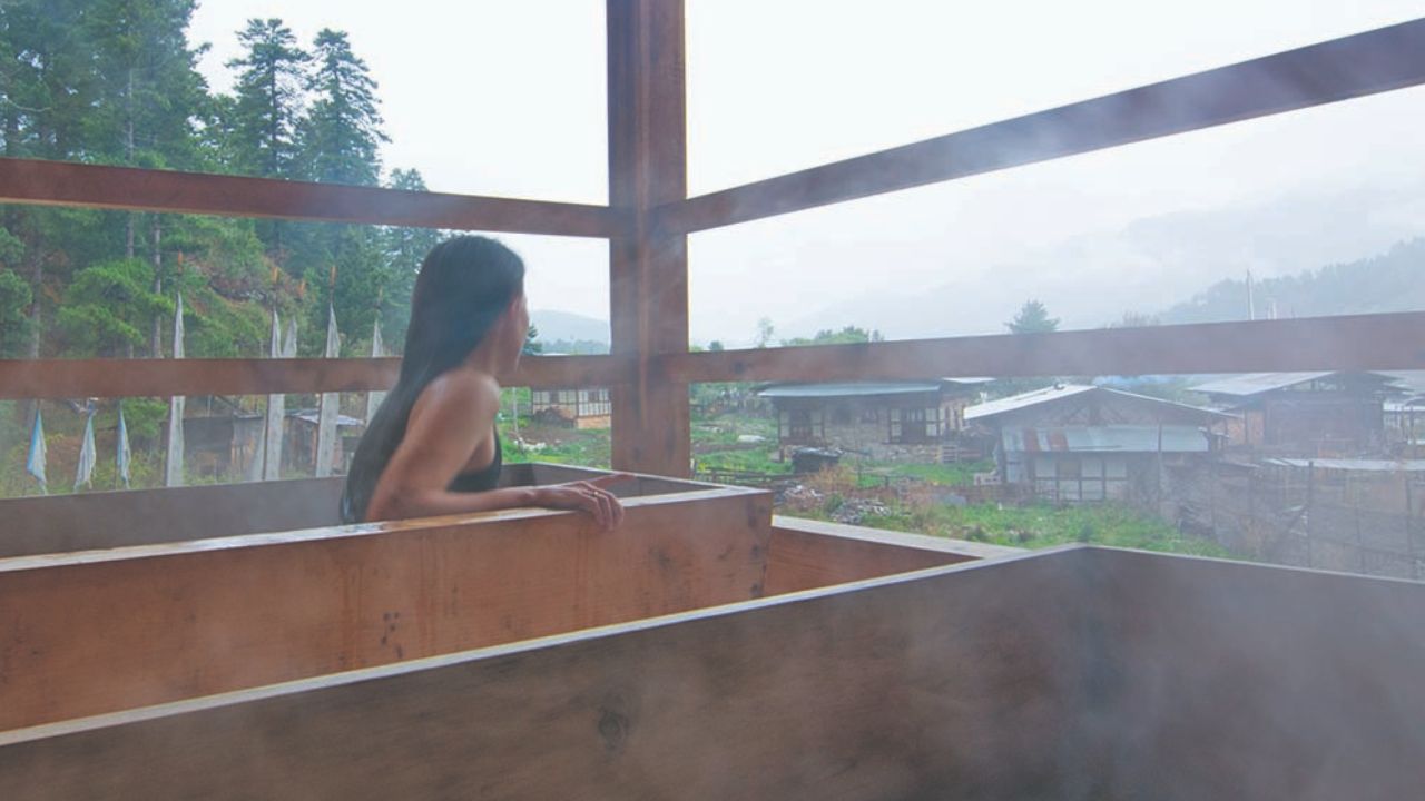 Woman relaxing in a traditional Bhutanese hot stone bath with mountain view