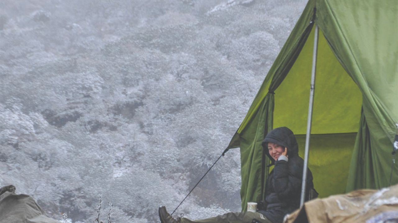 Hiker relaxing in a tent during cold mountain trekking conditions.