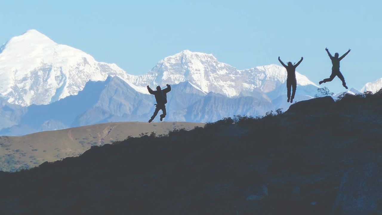 Three trekkers jumping on a ridge with snow-capped mountains in the background during the Jomolhari Trek in Bhutan.
